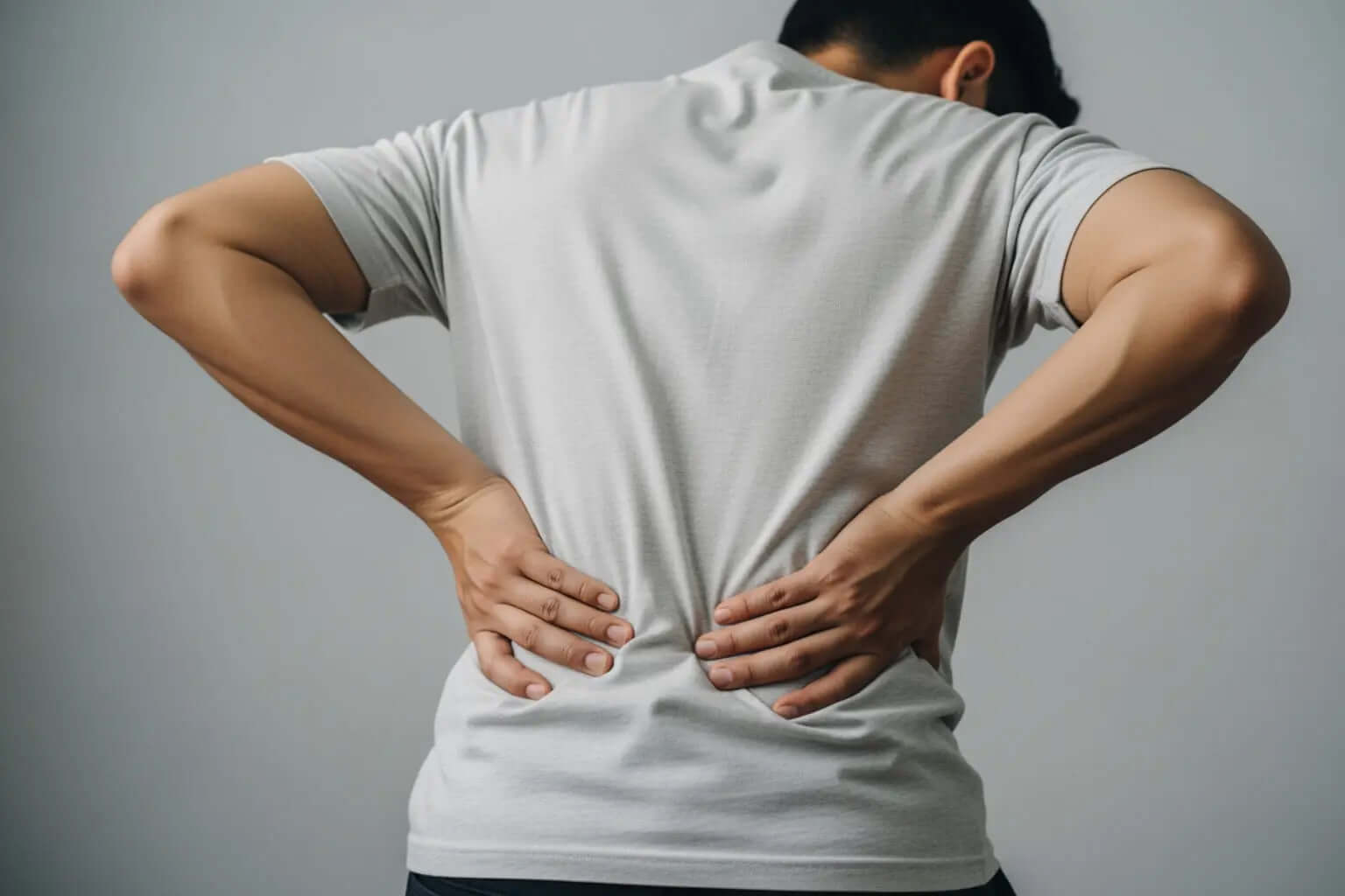 Man experiencing muscle strain relief for back pain, hands on lower back, in a gray shirt.